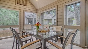 A covered outdoor dining area with a glass table and metal chairs, a vase with flowers, and a basket of bread. - Walk in minutes to Kiawah's famous beach! (Kiawah Island)