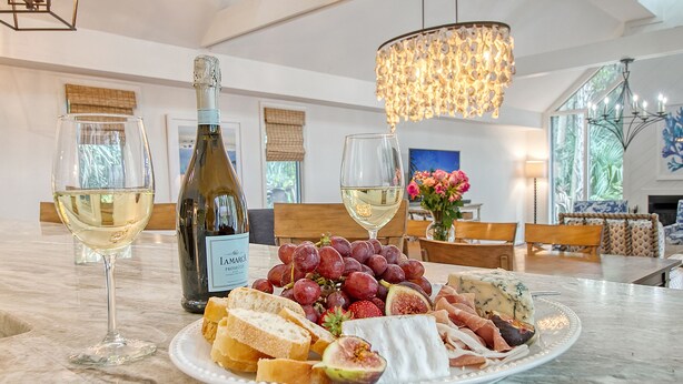 A dining table with a bottle of wine, two glasses of white wine, a plate of cheese, grapes, and bread. - Walk in minutes to Kiawah's famous beach! (Kiawah Island)