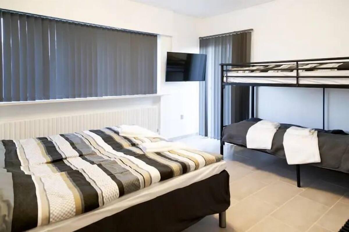 A hotel room with a single bed, a bunk bed, a flat-screen TV mounted on the wall, and a window with curtains.
