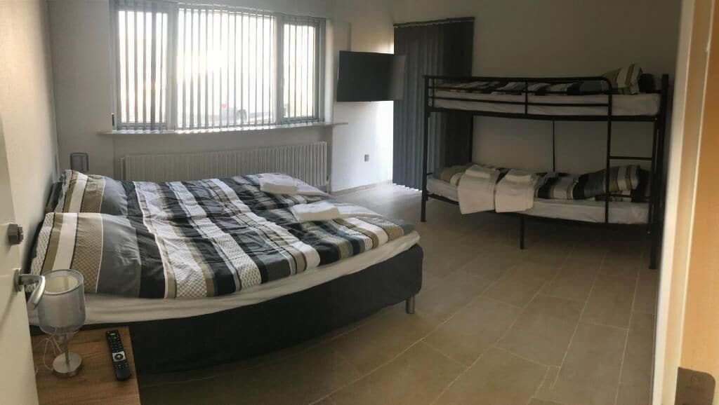 A bedroom with a large bed, a bunk bed, a TV, and a window with blinds.