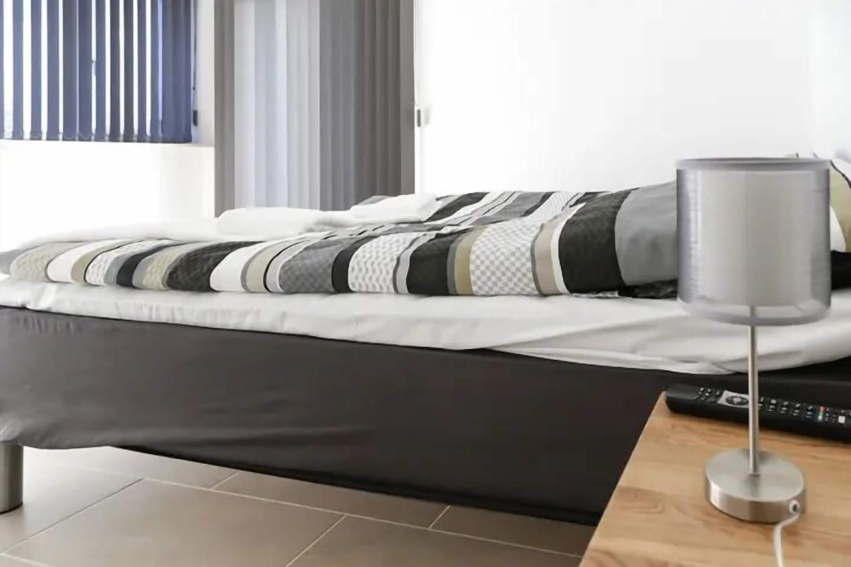 A modern bedroom with a bed, a bedside table with a lamp, and a remote control.