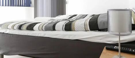 Un dormitorio moderno con una cama, una mesita de noche con lámpara y un control remoto.