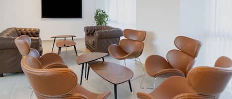 A modern room with leather sofas, a coffee table, and leather chairs. There is a TV mounted on the wall and a plant in the corner.