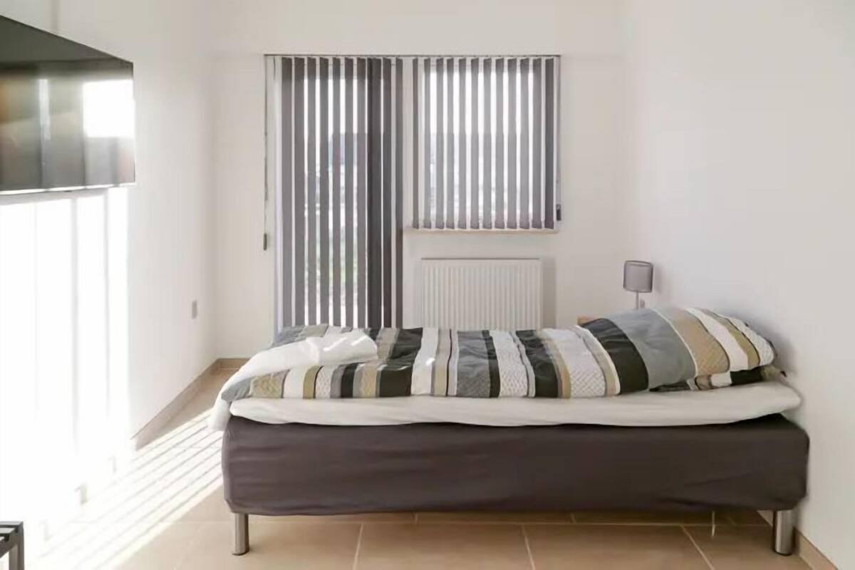 A bedroom with a bed, a radiator, a window with blinds, and a lamp on a bedside table.
