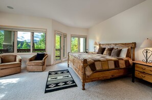 A bedroom with a large bed, two armchairs, a nightstand, and a view of a mountainous landscape through large windows. - Mountainscape Long Stay Townhome: 30+ Day Rental w/ Breathtaking Views (Breckenridge)