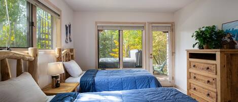 A bedroom with two beds, a wooden dresser, and a large window with a view of trees.