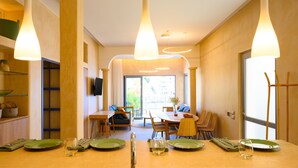 Un espace repas moderne avec une table en bois dressée pour deux personnes, un téléviseur fixé au mur et une vue sur l’extérieur grâce à une grande fenêtre.