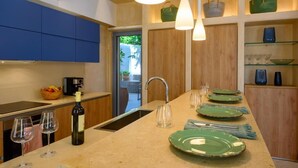 Une cuisine moderne avec des meubles bleus, un îlot central orné d’assiettes vertes, une bouteille de vin et des luminaires suspendus.