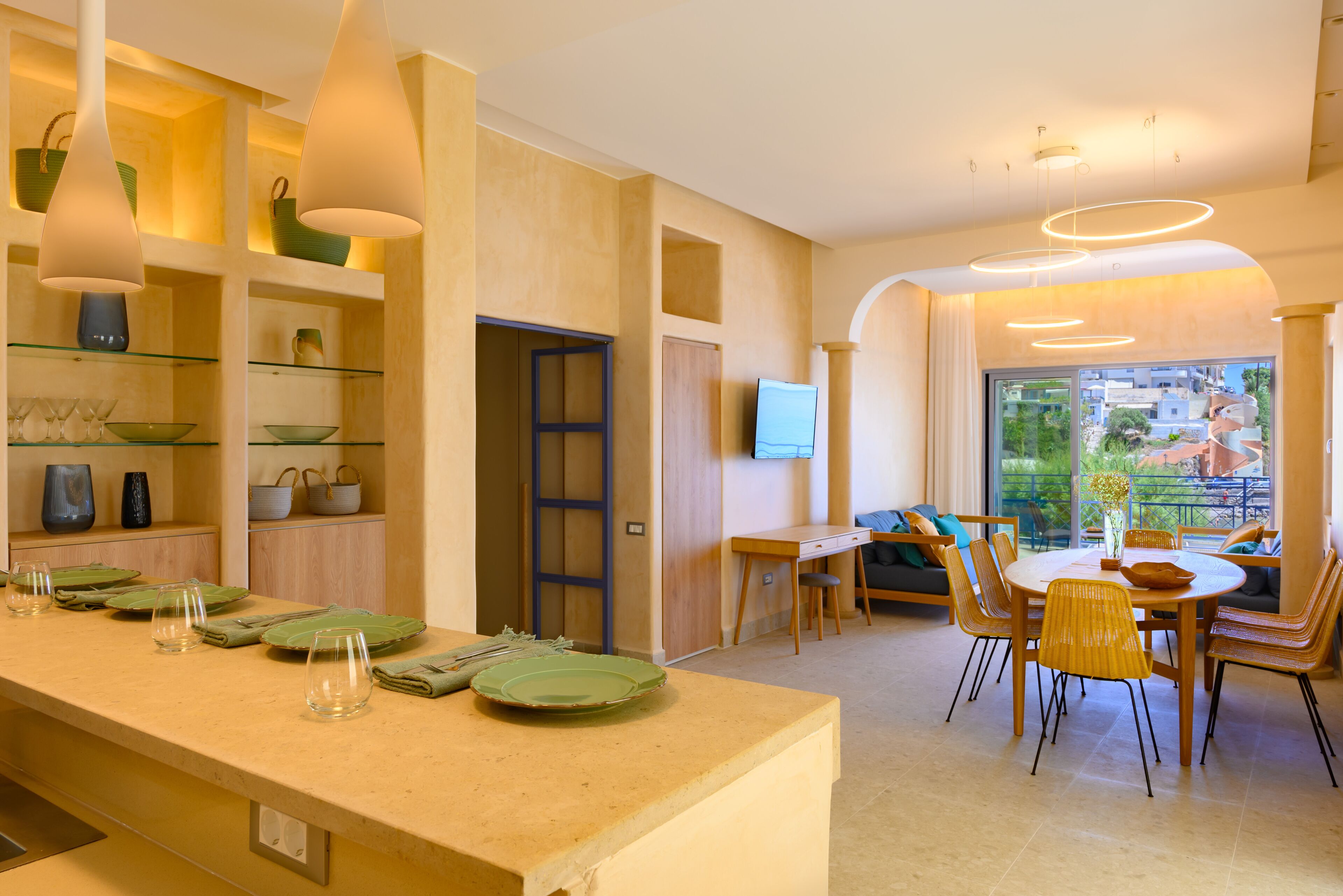 Eine moderne Küche mit Essbereich, ausgestattet mit einer langen Arbeitsplatte, Gläsern, einem Esstisch mit Stühlen und einem Fernseher an der Wand.