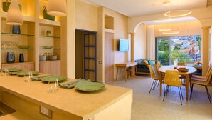 Une cuisine moderne avec un coin repas, comprenant un long comptoir avec de la verrerie, une table à manger avec des chaises et un téléviseur fixé au mur.