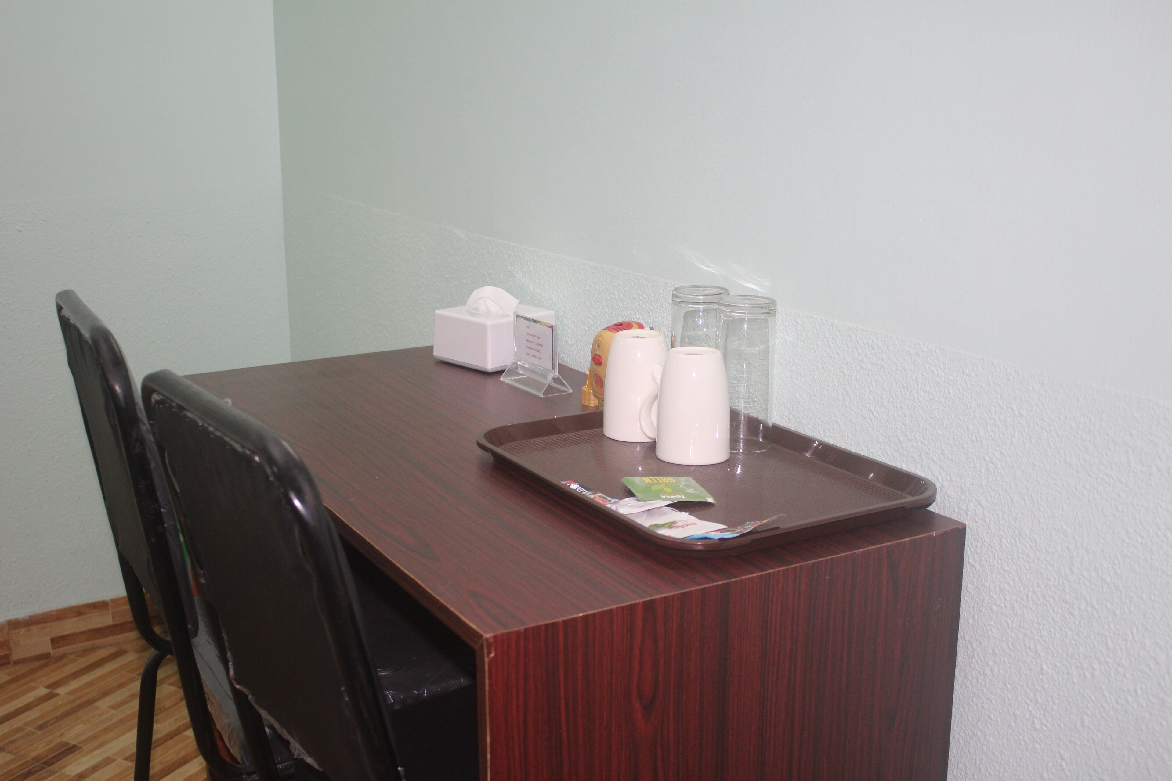 A wooden desk with a tray containing a tissue box, a small bottle, and two white mugs.