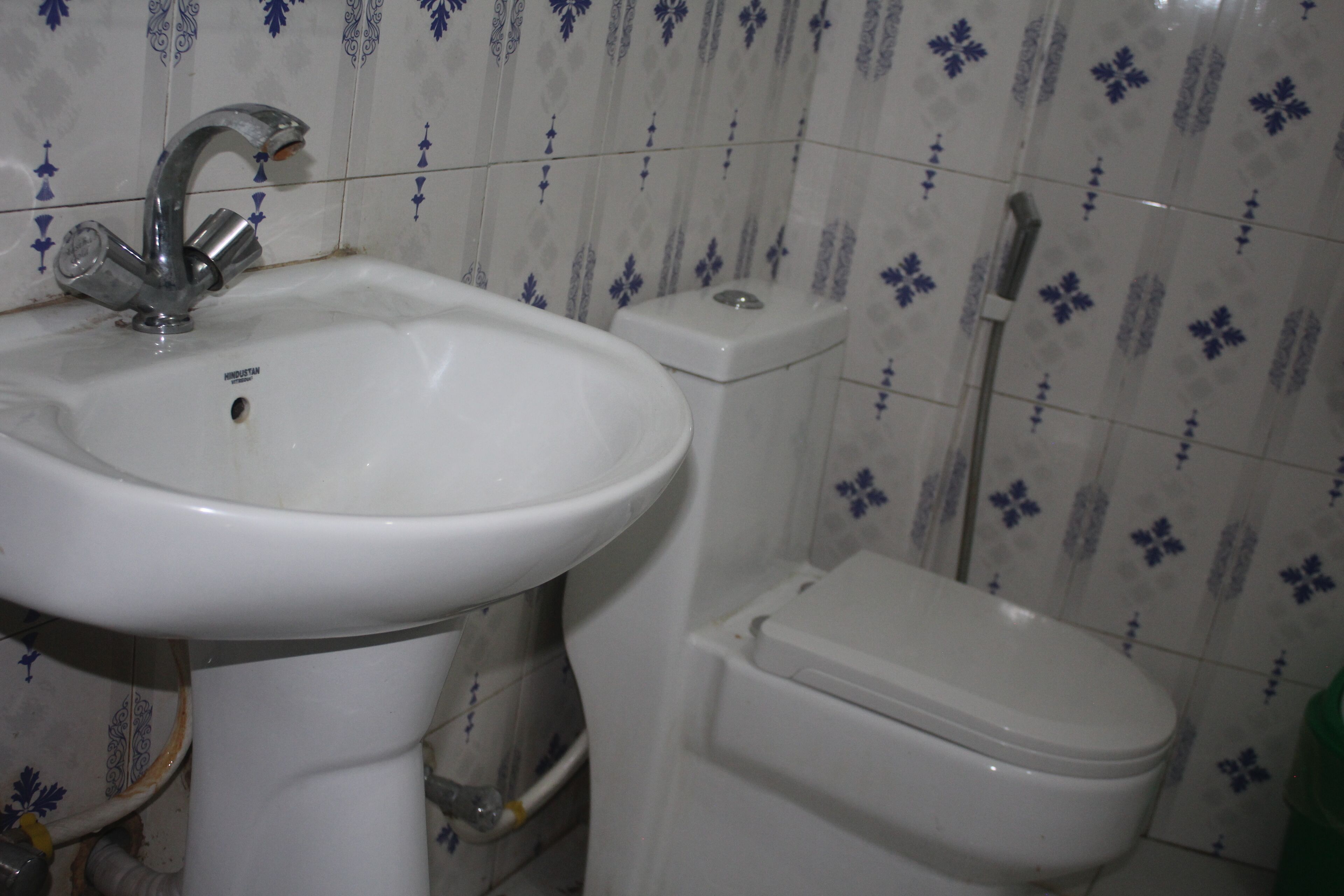 A bathroom with a white sink, toilet, and shower. The walls have a blue and white patterned tile design.