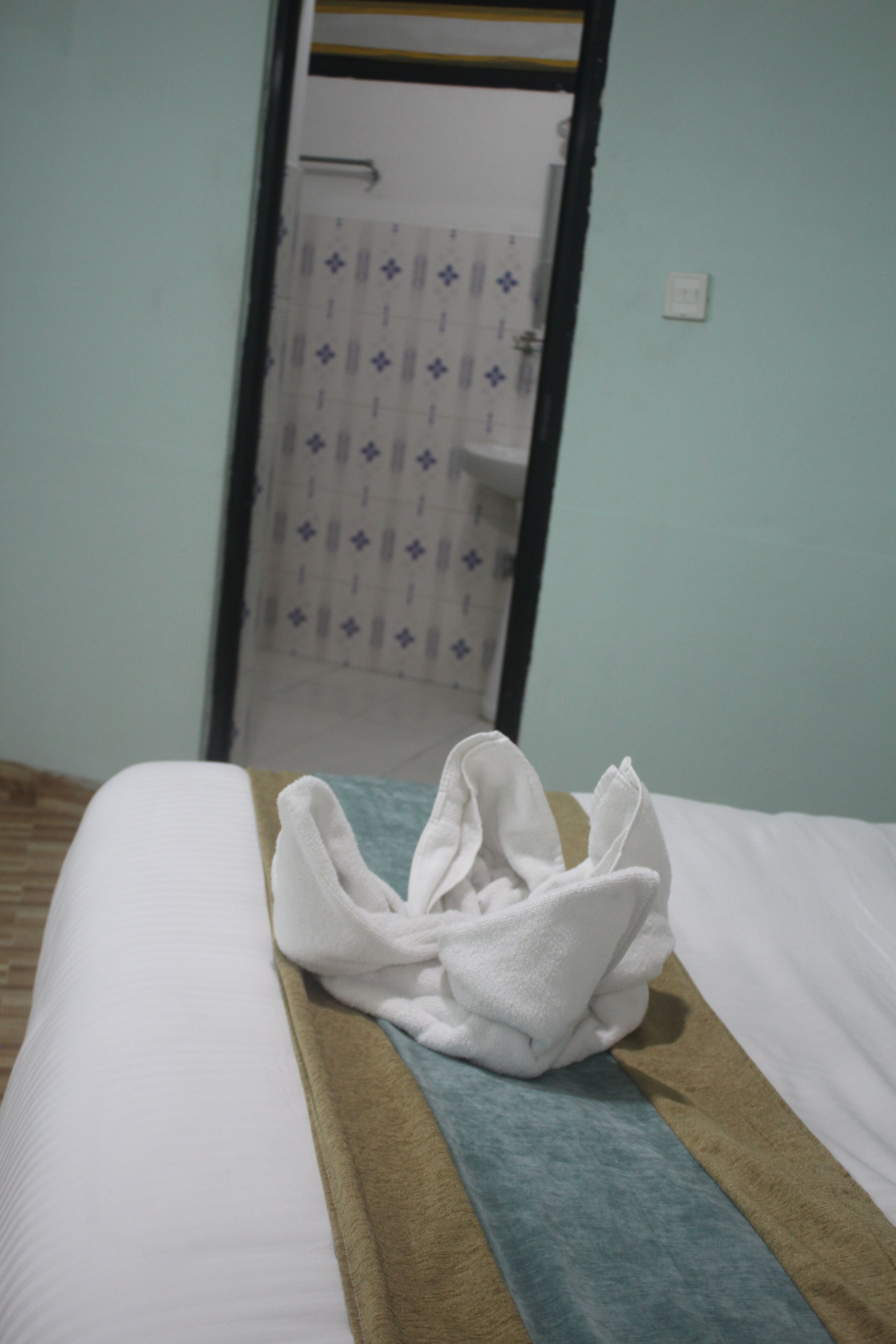 A neatly made bed with a white and brown blanket, a white towel, and a blue towel on the bed.