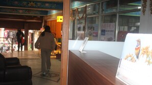 A reception area with a wooden counter, a poster, and a window with posters. - Yaksa Hotel Pvt. Ltd. (Kathmandu)