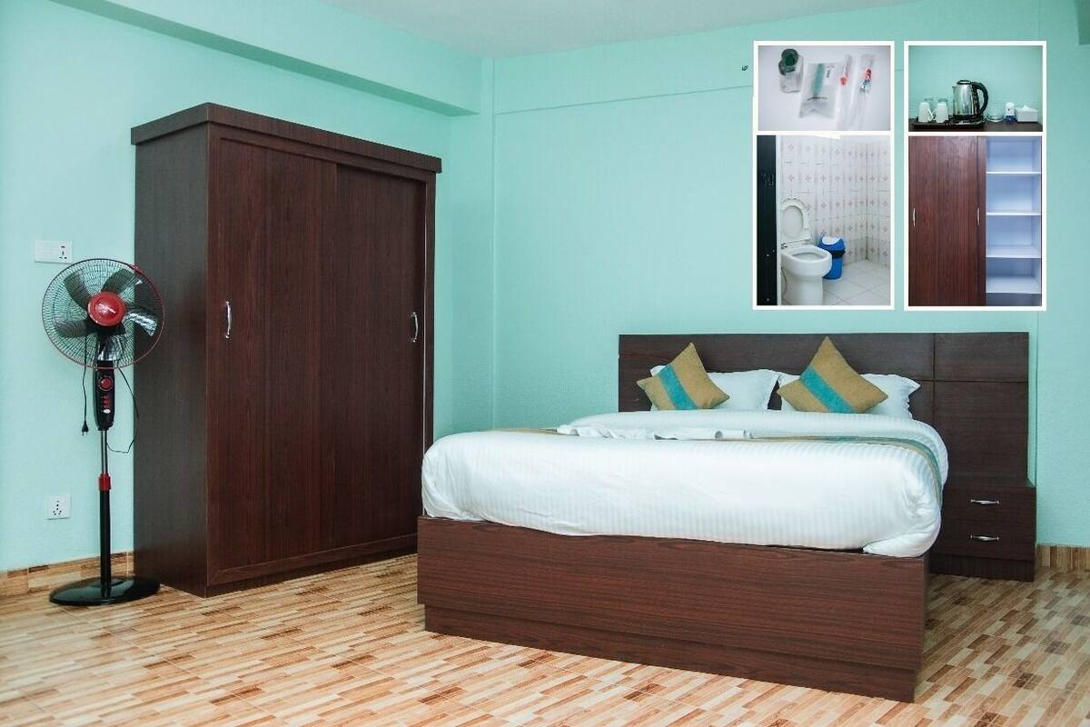 Un dormitorio con un armario grande, una cama con almohadas, un ventilador de pie y un baño pequeño con inodoro y lavamanos.
