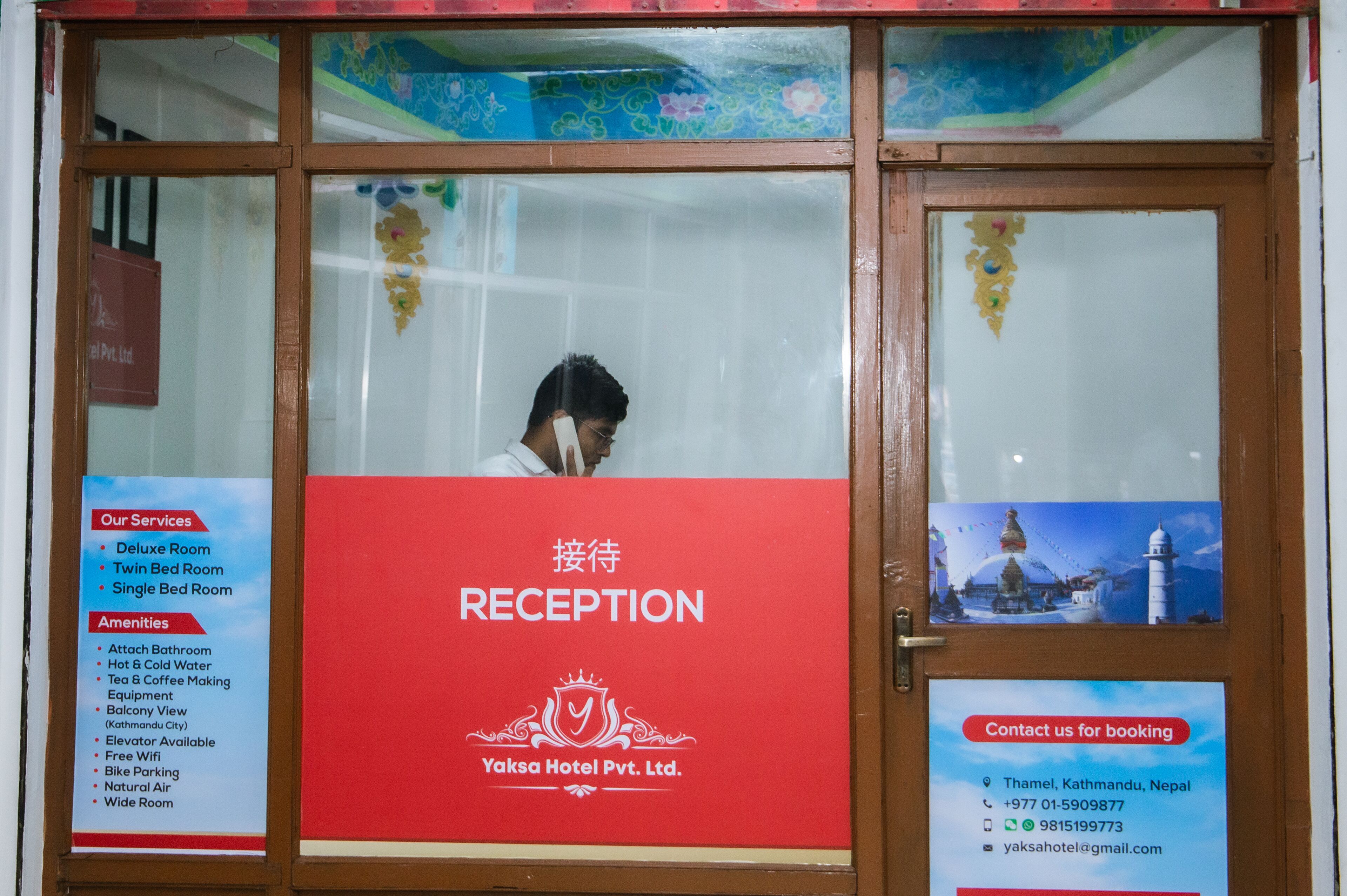 A reception area with a sign indicating services and amenities, including deluxe, twin, and single bed rooms, bathroom facilities, hot & cold water, tea & coffee making equipment, balcony view, elevator, free wifi, bike parking, natural air, and wide rooms.