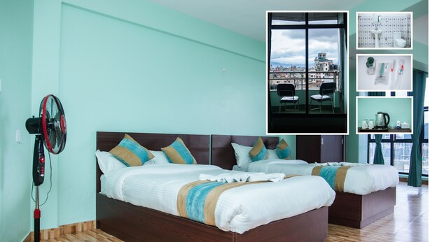A hotel room with two beds, a standing fan, and a view of the city through large windows. - Yaksa Hotel Pvt. Ltd. (Kathmandu)