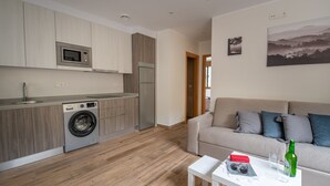 A compact living space with a kitchenette, a washing machine, a sofa, and a coffee table. - Apartamentos Las Caldas . Castillo de Priorio , 15 Minutos del Centro de Oviedo (Priorio)
