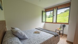 A bedroom with a large bed, a window with a view of a green landscape, and a chair with a bouquet of flowers. - Apartamentos Las Caldas . Castillo de Priorio , 15 Minutos del Centro de Oviedo (Priorio)