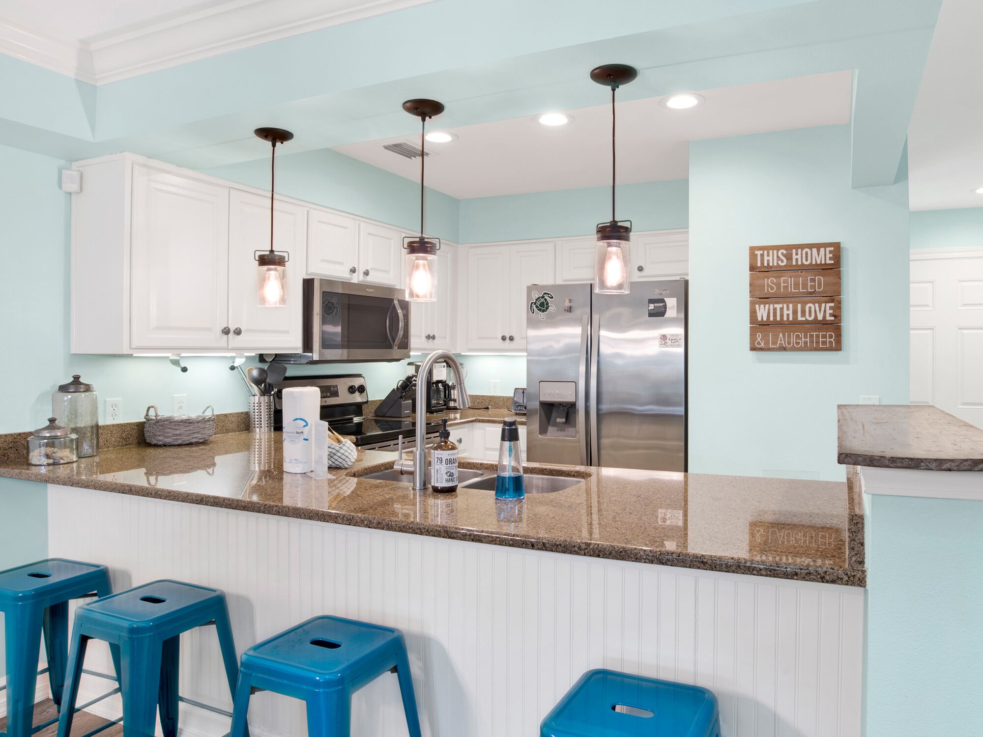 A modern kitchen with white cabinets, stainless steel appliances, and blue bar stools.
