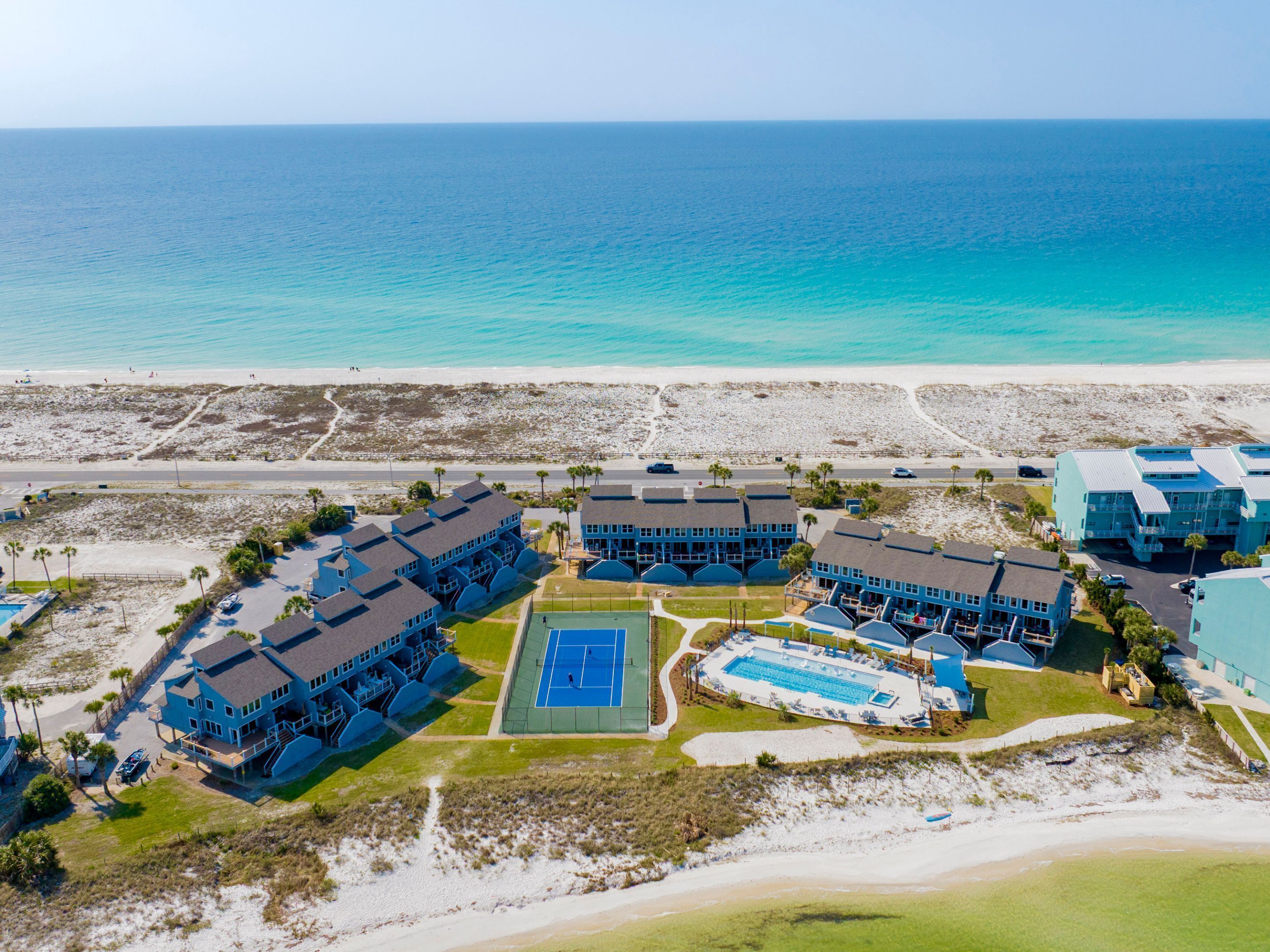 A resort with multiple blue buildings, a tennis court, and a beach view.