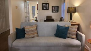 A living room with a sofa, two patterned pillows, a table with a laptop, and framed artwork on the wall. - Elegance & Style With Custom Canopy Beds (Halifax)