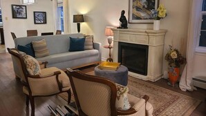 Een woonkamer met een bank, fauteuils, een open haard en een schilderij aan de muur.