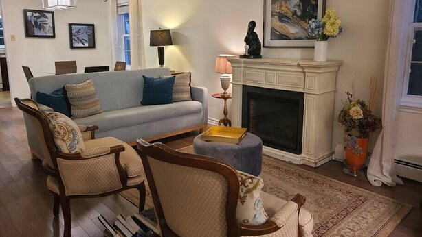 A living room with a sofa, armchairs, a fireplace, and a painting on the wall. - Elegance & Style With Custom Canopy Beds (Halifax)