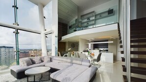 A modern living room with a sectional sofa, a dining area, and a kitchen. - Amazing Skyline Views 3BR Duplex (Manchester)