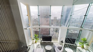 A modern living room with a sofa, two round tables, a TV, and potted plants. - Amazing Skyline Views 3BR Duplex (Manchester)