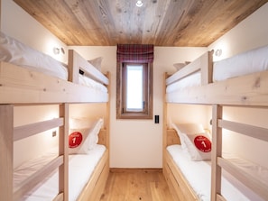 A room with two bunk beds, a small window with a plaid curtain, and a wooden ceiling.