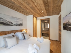 A bedroom with a wooden ceiling, a bed with white linens, and two paintings on the walls.