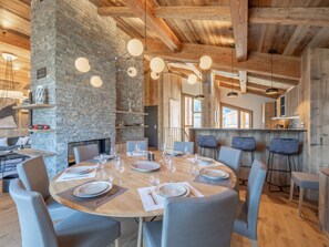 A dining area with a stone wall, wooden ceiling beams, and a round table set for six. - Family chalet with pool and pets allowed near slopes (Courchevel)