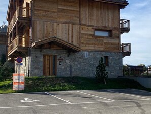 A wooden building with balconies, a stone base, and a parking area with a handicapped parking space.