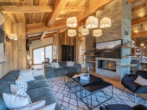 A cozy living room with a fireplace, wooden beams, and a stone wall.