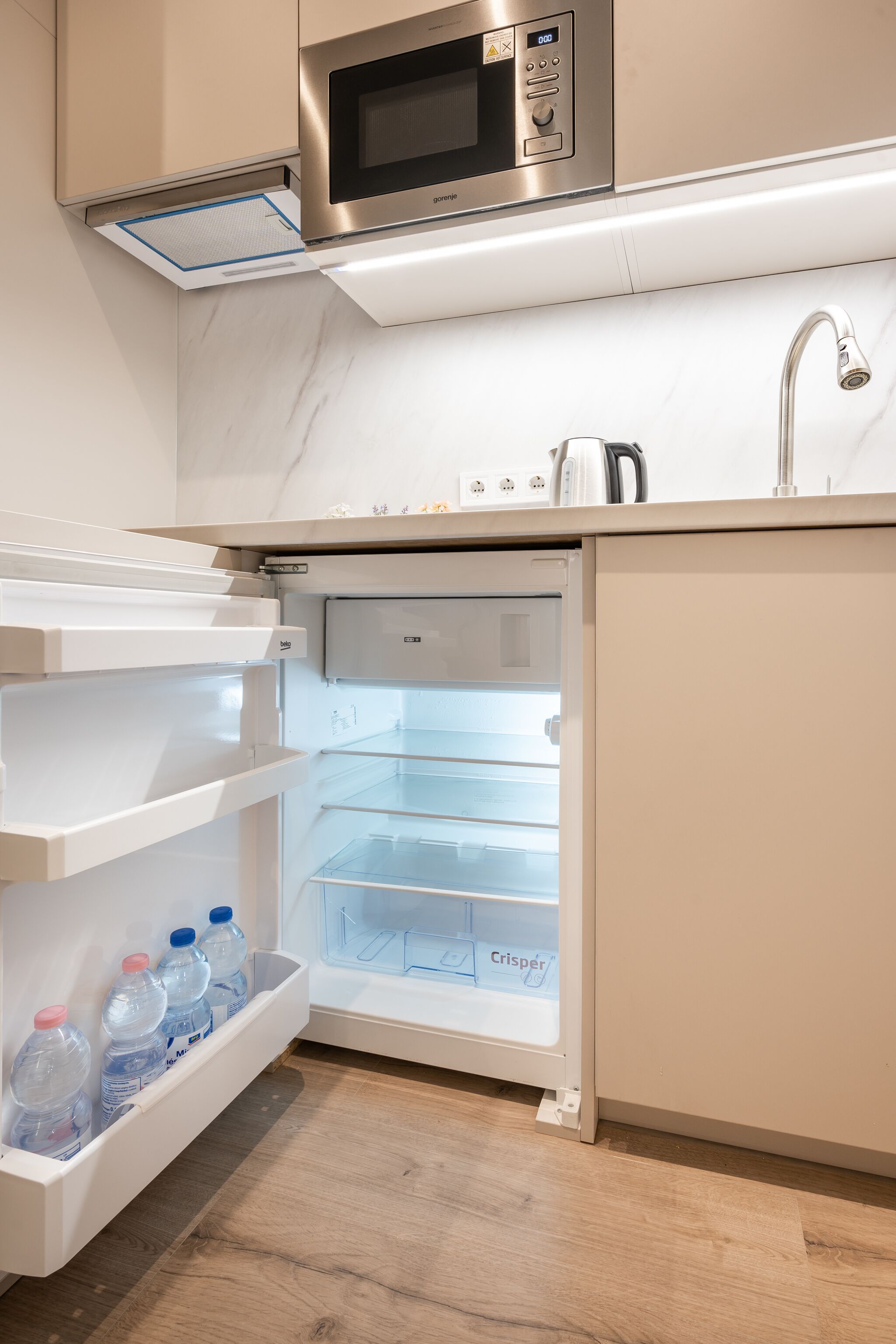 A compact kitchen with a built-in microwave, a stainless steel sink, and a refrigerator with a water dispenser.
