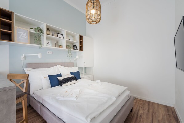 Une chambre moderne comprenant un lit, des tables de chevet, un téléviseur fixé au mur et des étagères intégrées ornées d’objets décoratifs.