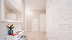Un pasillo con pared de ladrillo blanco, una puerta blanca y una consola blanca con un florero y revistas.