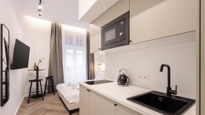 Habitación de hotel compacta con kitchenette, una cama, televisor y ventana con cortinas.
