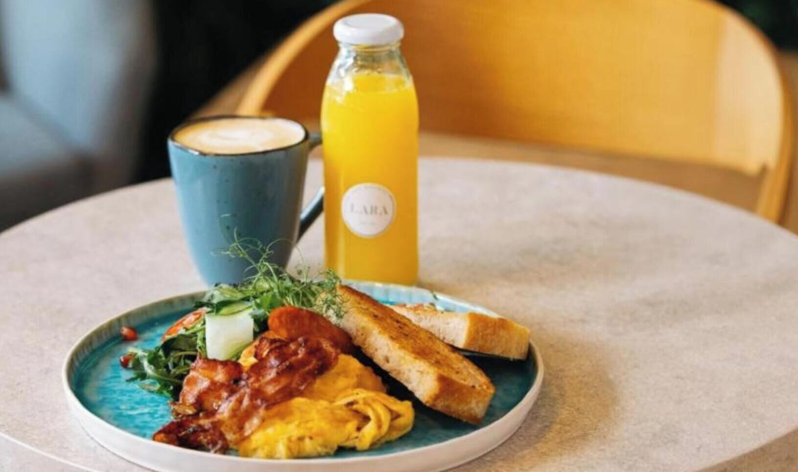 A breakfast plate with toast, scrambled eggs, bacon, and a cup of coffee.
