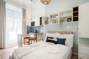 A modern bedroom with a bed, bedside tables, a desk, and a kitchenette. - A13 - Boutique Apartments by BQA (Budapest)