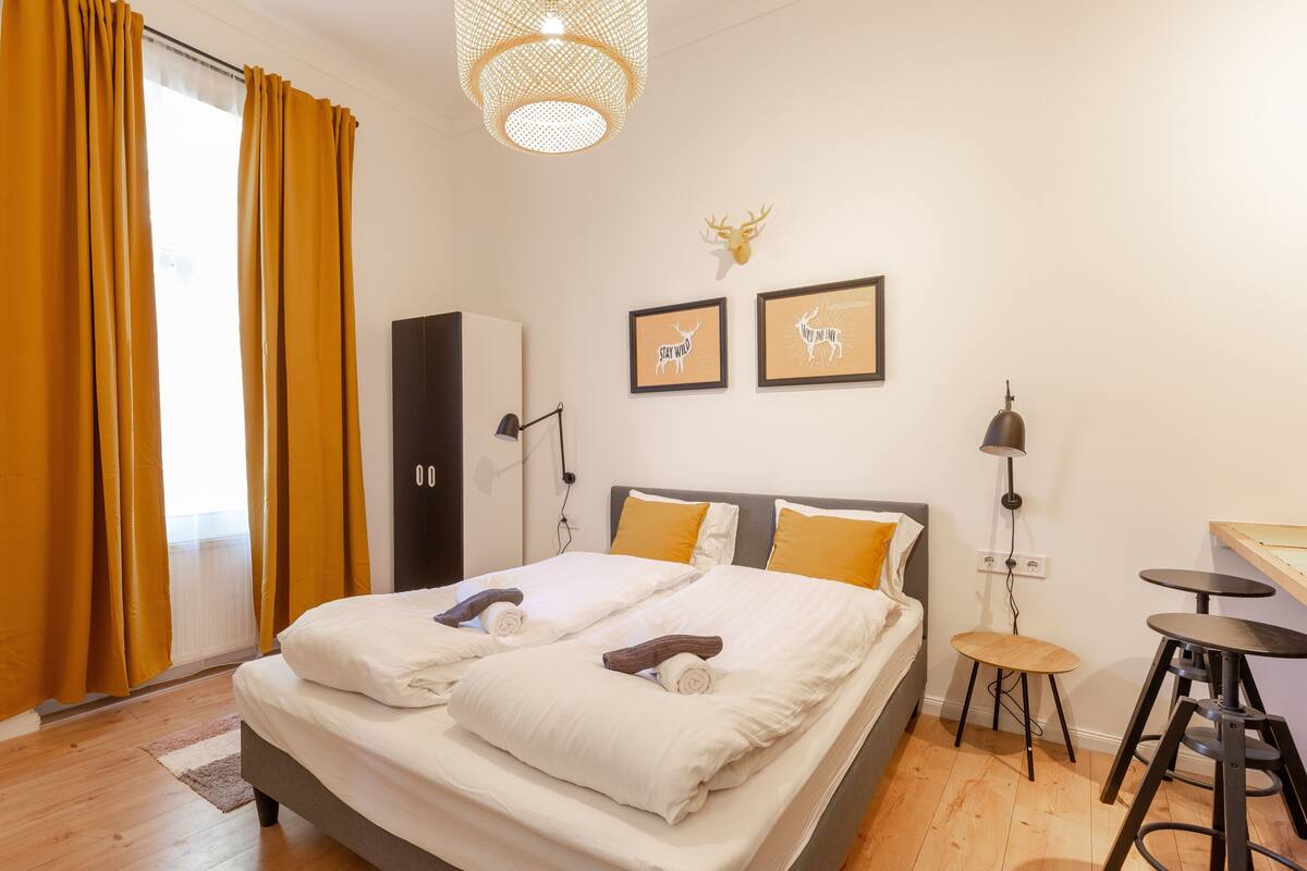 Une chambre d’hôtel comprenant un lit, deux tables de chevet, une armoire, un lustre et deux tableaux encadrés accrochés au mur.