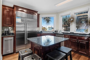A modern kitchen with a stainless steel refrigerator, wooden cabinets, granite countertops, and a large island with stools.