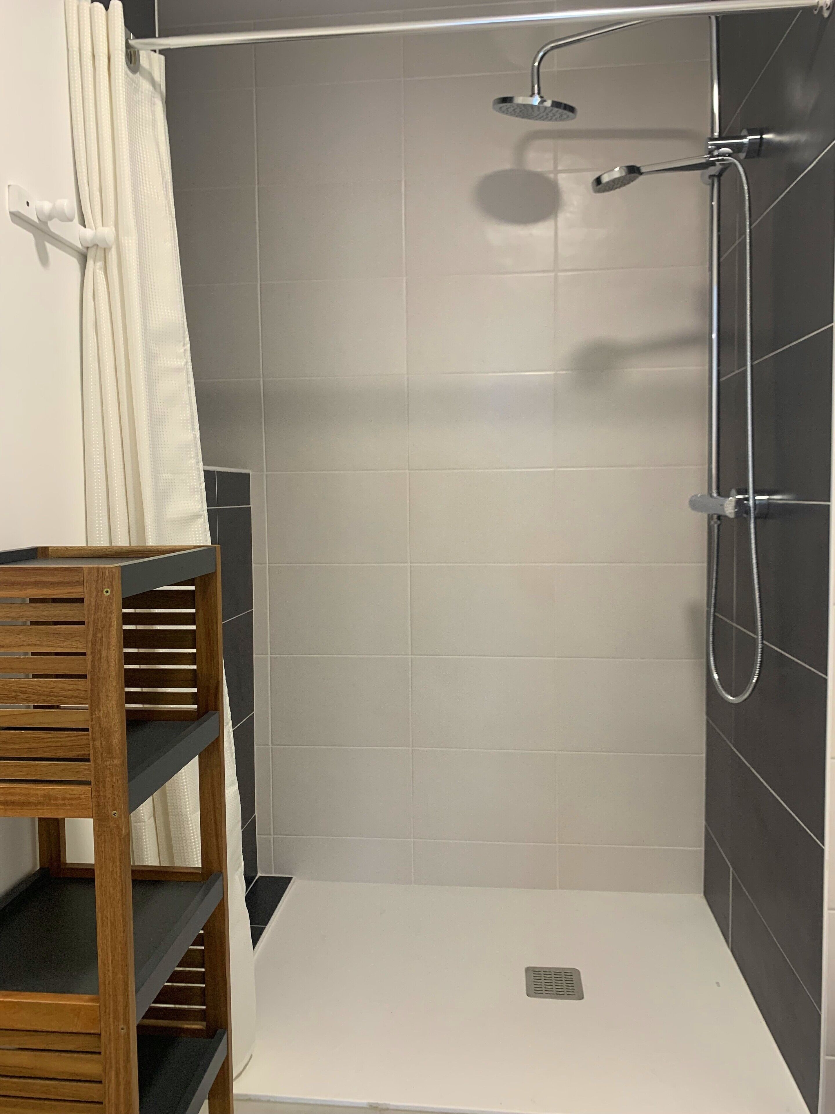 Un espace douche avec un mur recouvert de carreaux blancs, une pomme de douche et un pommeau de douche amovible.