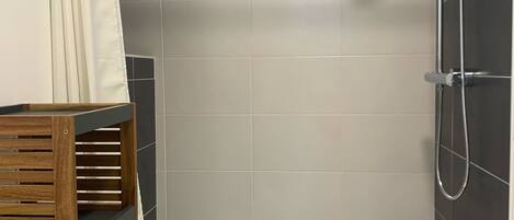Un espace douche avec un mur recouvert de carreaux blancs, une pomme de douche et un pommeau de douche amovible.