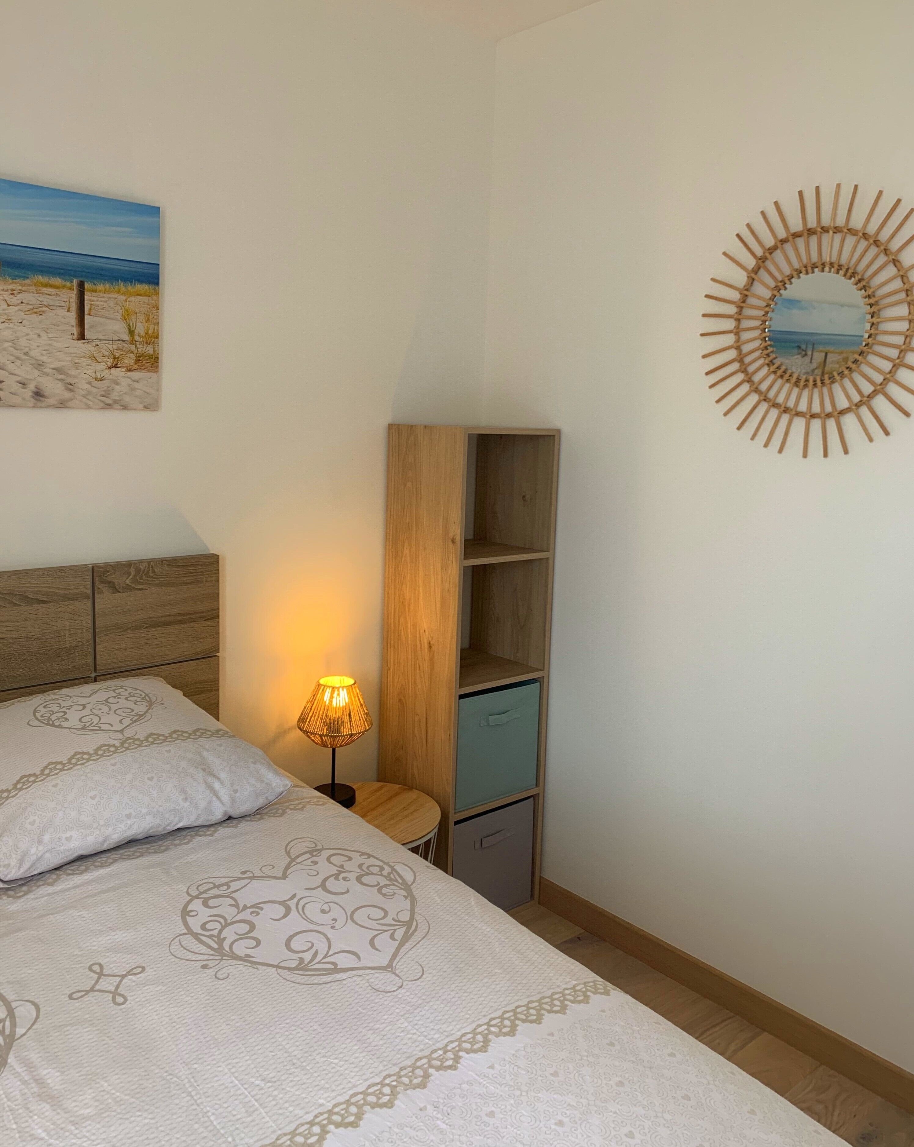 Een slaapkamer met een bed, nachtkastje, lamp, houten garderobe en een spiegel aan de muur.