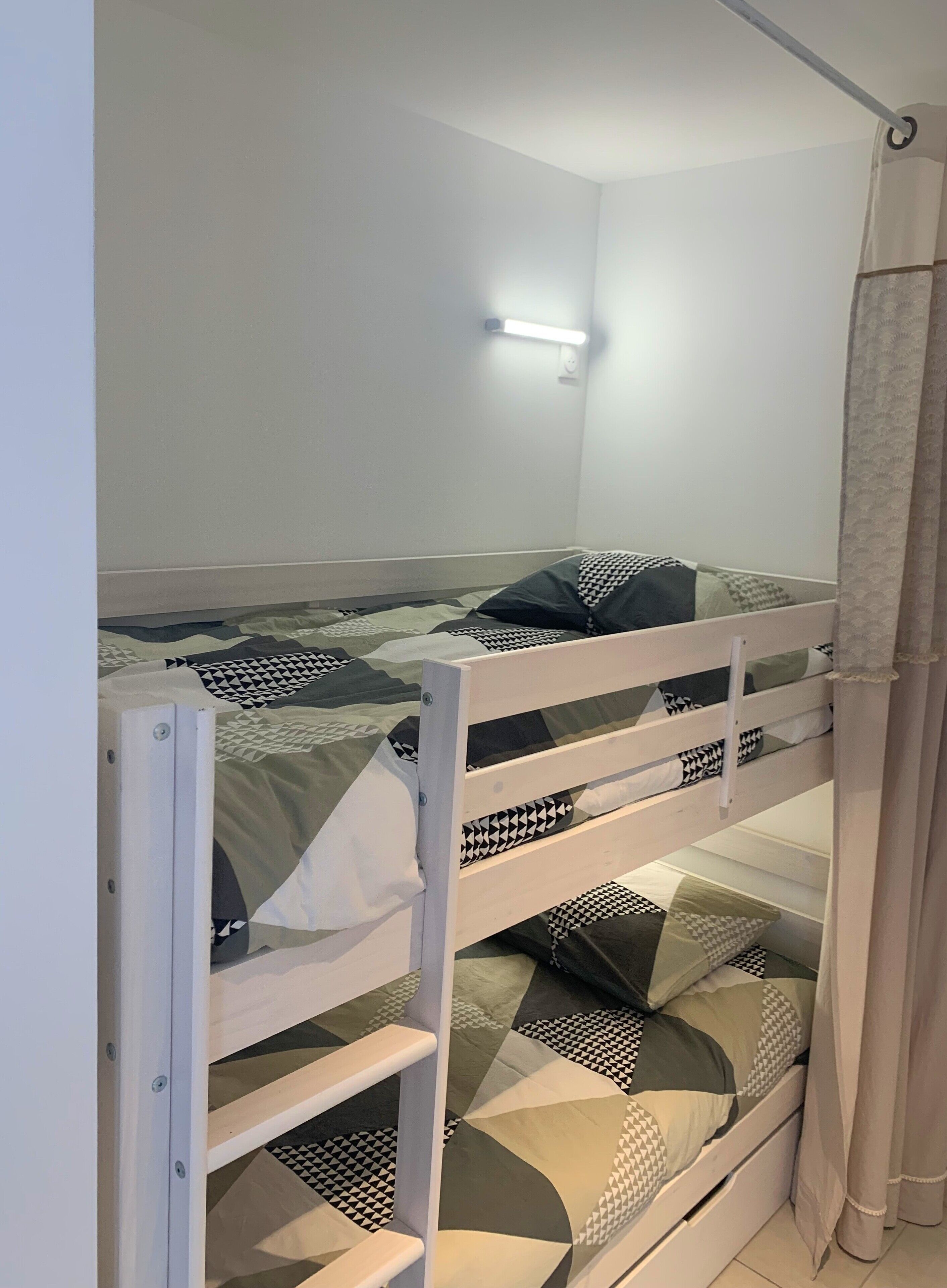 A bunk bed with geometric patterned bedding, a wall-mounted light, and a curtain.