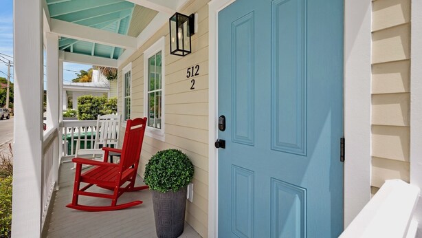 A porch with a red rocking chair, a potted plant, and a blue door with the number 512.
