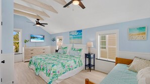 A bedroom with a bed, a desk, a chair, a ceiling fan, and a window.