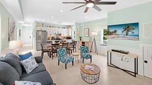 Ein modernes Wohnzimmer mit einer Couch, Sesseln, einem Couchtisch, einem Fernseher und einer Küche im Hintergrund.
